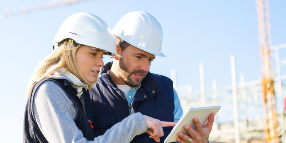 Two people on a construction site look at a digital work tablet.