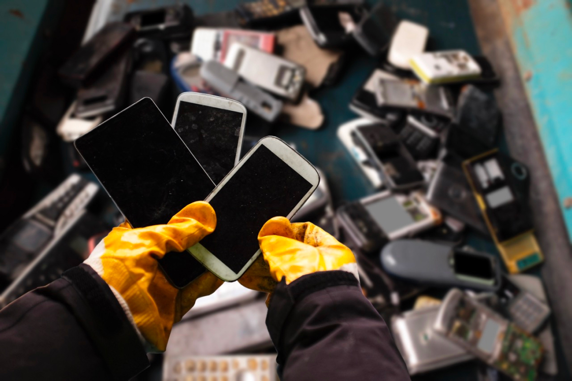 Une personne avec des gants orange trie de dizaines de téléphones mobiles.