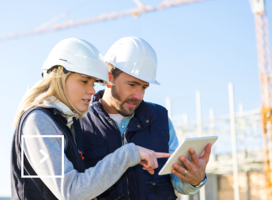 Two people on a construction site are looking at a digital work tablet.  
