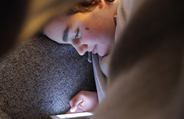 A young person sitting on her sofa looks at her mobile phone. 