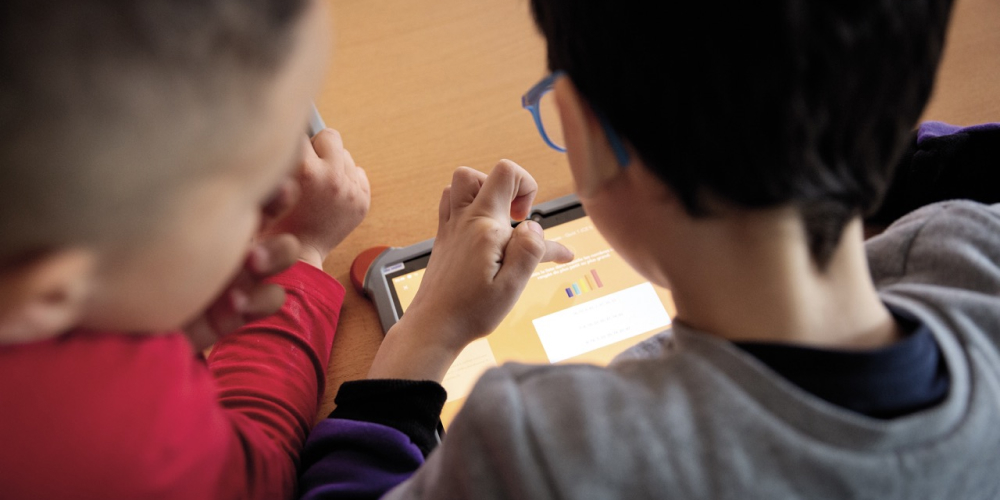 Deux jeunes élèves travaillent ensemble sur une tablette numérique. 