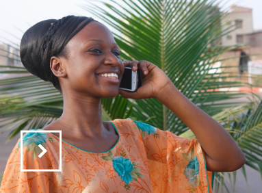 Une femme africaine avec une robe orange et bleue est au téléphone. 