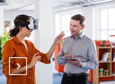 Une personne essaye un casque de réalité virtuel sous l’œil d’une tierce personne ayant en main une tablette numérique